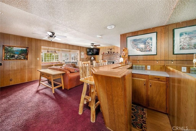 bar featuring a ceiling fan, carpet, a textured ceiling, and wooden walls