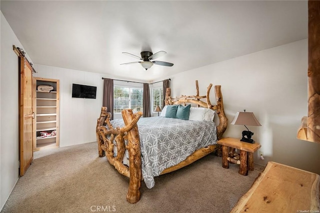 carpeted bedroom with a barn door, a spacious closet, and a ceiling fan