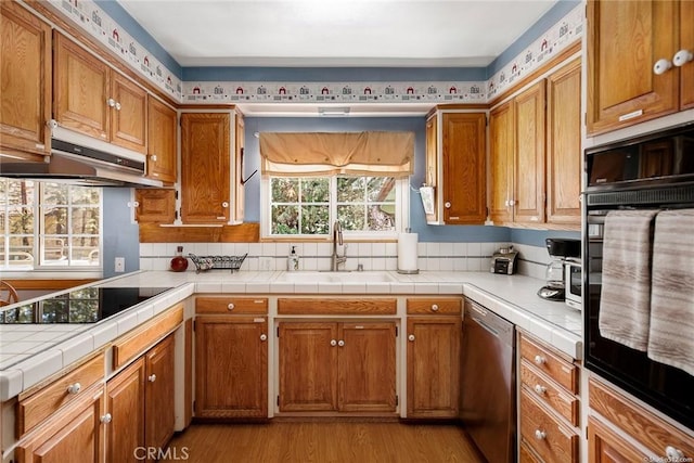 kitchen with black appliances, under cabinet range hood, brown cabinets, and a sink