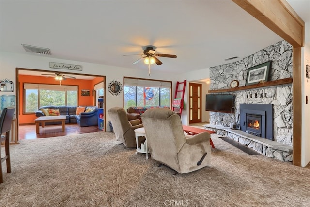 living area featuring visible vents, carpet flooring, a ceiling fan, and a stone fireplace