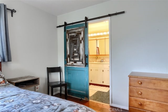 bedroom featuring a sink, a barn door, connected bathroom, and wood finished floors