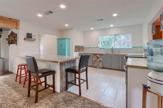 kitchen with gray cabinetry, a peninsula, a sink, visible vents, and a kitchen breakfast bar