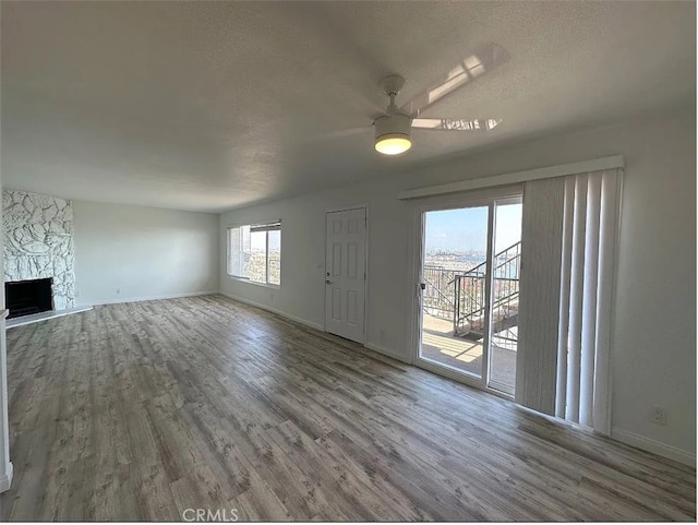 unfurnished living room featuring a fireplace, a textured ceiling, baseboards, and wood finished floors