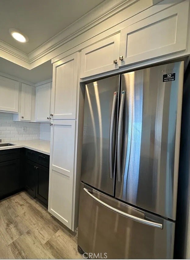 kitchen with tasteful backsplash, light countertops, ornamental molding, freestanding refrigerator, and white cabinetry