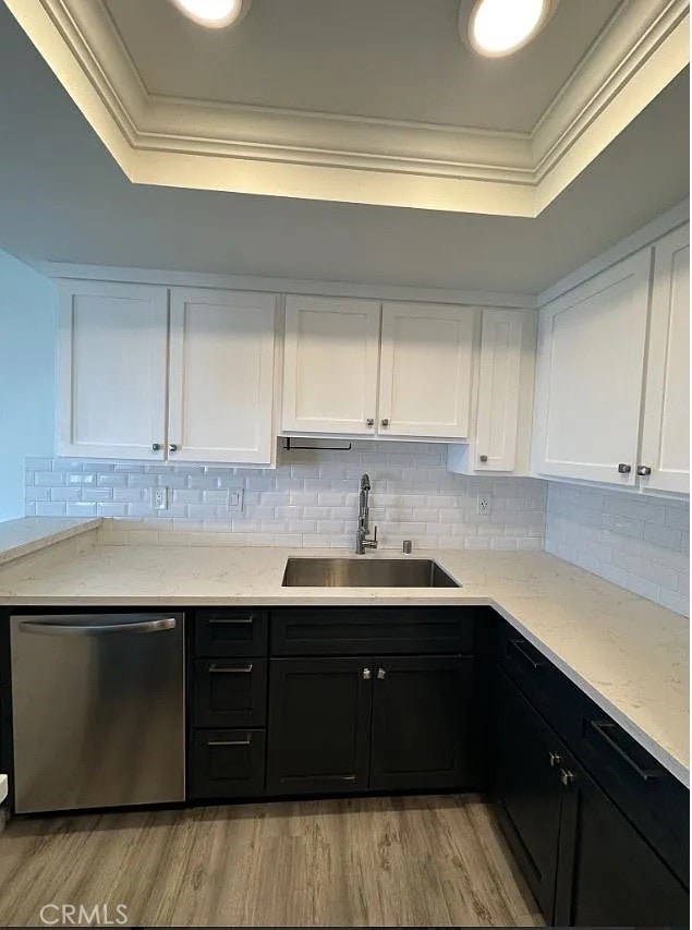 kitchen with a sink, crown molding, a tray ceiling, and dishwasher