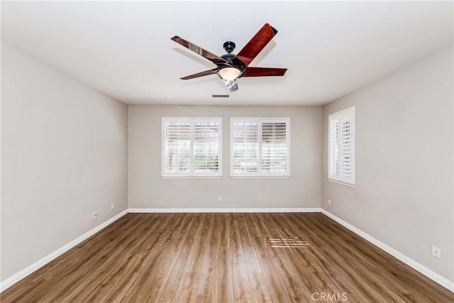 empty room featuring a ceiling fan, visible vents, baseboards, and wood finished floors