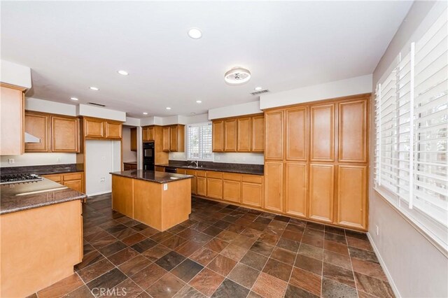 kitchen with dark countertops, a kitchen island, stone finish floor, a sink, and recessed lighting