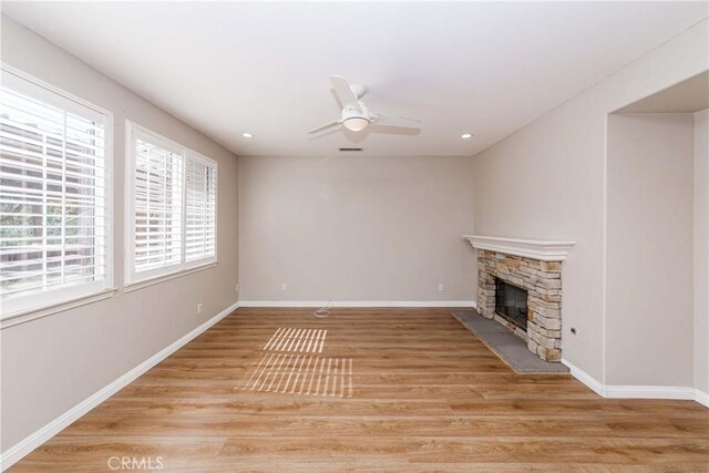 unfurnished living room featuring a stone fireplace, light wood-style flooring, recessed lighting, a ceiling fan, and baseboards