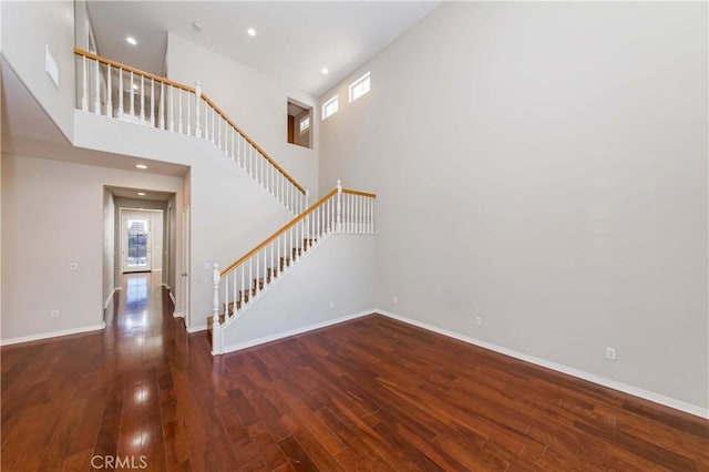 interior space featuring wood-type flooring, a high ceiling, baseboards, and recessed lighting