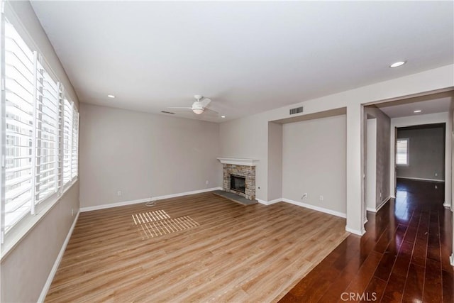 unfurnished living room with a fireplace, visible vents, ceiling fan, wood finished floors, and baseboards