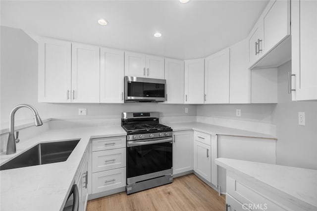 kitchen featuring appliances with stainless steel finishes, light wood finished floors, a sink, and white cabinets
