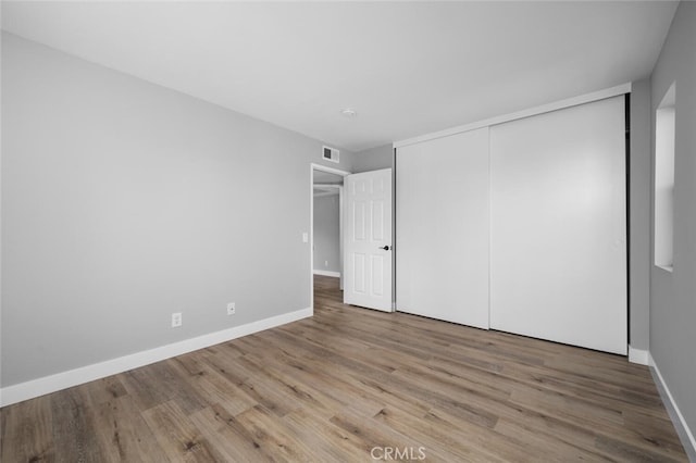unfurnished bedroom featuring visible vents, a closet, baseboards, and wood finished floors