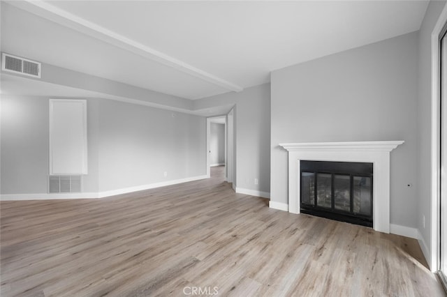 unfurnished living room with a glass covered fireplace, visible vents, baseboards, and wood finished floors