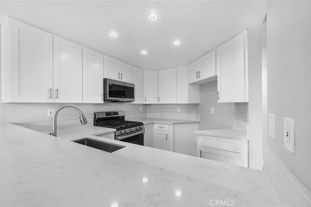 kitchen with appliances with stainless steel finishes, white cabinetry, a sink, and light stone countertops