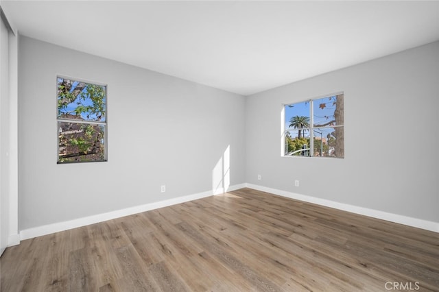 unfurnished room featuring baseboards, wood finished floors, and a healthy amount of sunlight