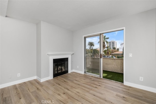 unfurnished living room with a glass covered fireplace, baseboards, and wood finished floors