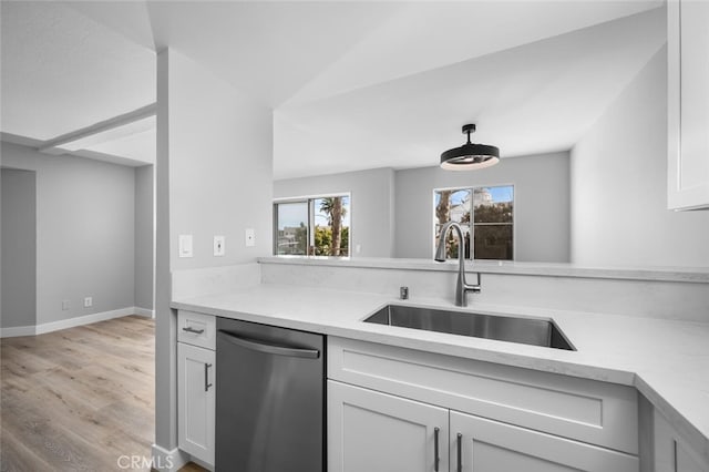 kitchen with light countertops, white cabinets, stainless steel dishwasher, light wood finished floors, and a sink
