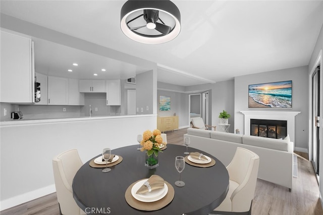 dining space featuring recessed lighting, light wood-style flooring, baseboards, and a glass covered fireplace