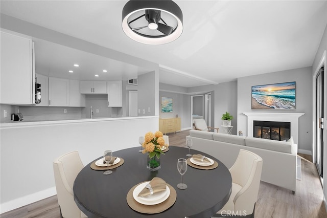 dining room featuring light wood-style flooring, recessed lighting, a glass covered fireplace, and baseboards