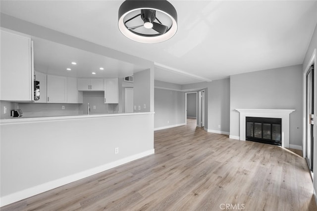 unfurnished living room featuring recessed lighting, a glass covered fireplace, a sink, light wood-type flooring, and baseboards