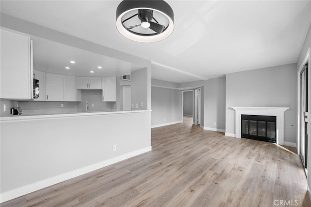 unfurnished living room with light wood-style flooring, a sink, baseboards, and recessed lighting
