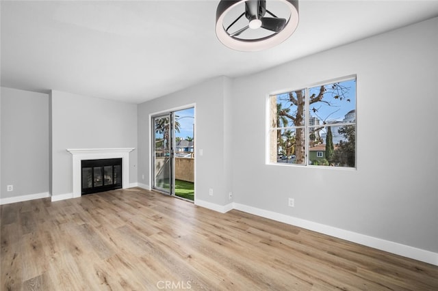 unfurnished living room with wood finished floors, a glass covered fireplace, a ceiling fan, and baseboards