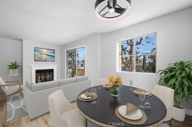 dining space with light wood-type flooring, plenty of natural light, and a glass covered fireplace