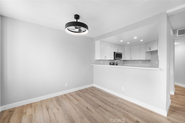 kitchen featuring baseboards, stainless steel microwave, light countertops, and light wood-style flooring