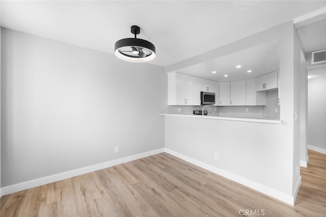 kitchen featuring light wood-style flooring, white cabinetry, stainless steel microwave, light countertops, and baseboards