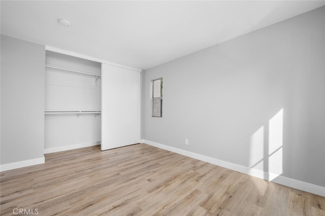 unfurnished bedroom featuring light wood finished floors, baseboards, and a closet