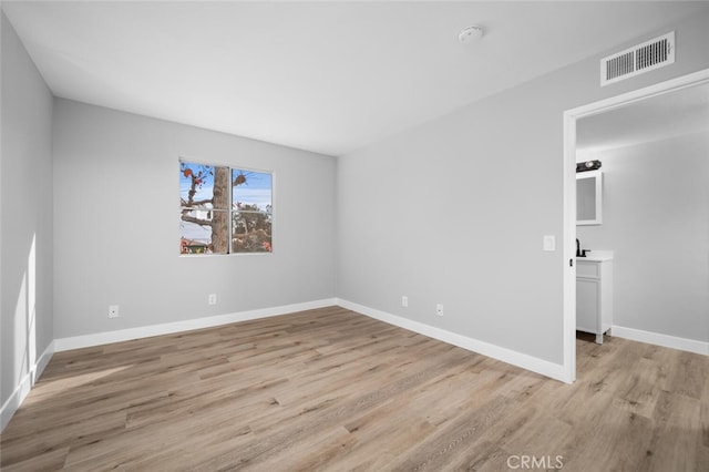 spare room with light wood finished floors, visible vents, and baseboards