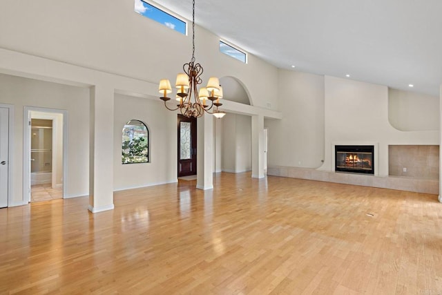 unfurnished living room with baseboards, a glass covered fireplace, a towering ceiling, light wood-style flooring, and a chandelier