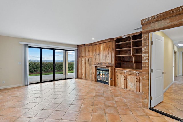 unfurnished living room with light tile patterned floors, visible vents, built in features, baseboards, and a glass covered fireplace