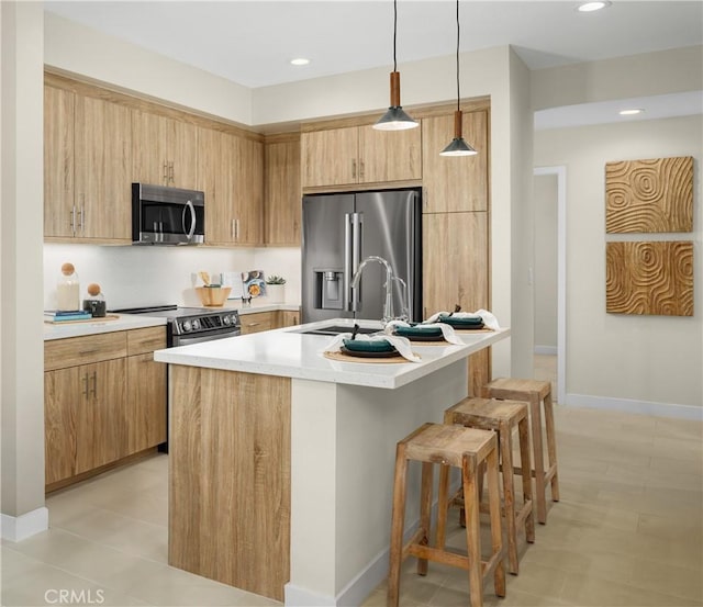 kitchen with a sink, a kitchen breakfast bar, light countertops, appliances with stainless steel finishes, and hanging light fixtures