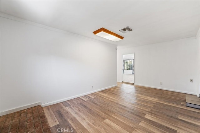 unfurnished room with crown molding, wood finished floors, visible vents, and baseboards