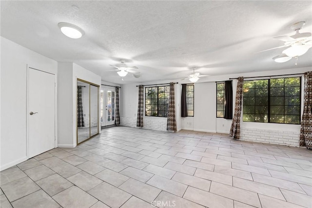 interior space with baseboards, a textured ceiling, brick wall, and a ceiling fan