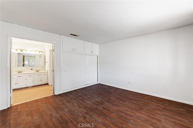 unfurnished bedroom with visible vents, baseboards, ensuite bathroom, wood finished floors, and a closet