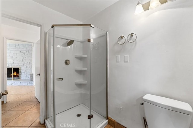 bathroom featuring tile patterned floors, toilet, a stone fireplace, and a shower stall