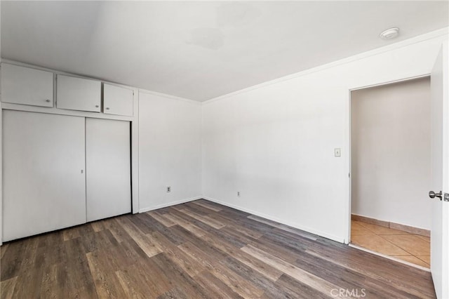 unfurnished bedroom with a closet, baseboards, and dark wood-style floors