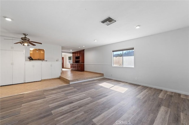 unfurnished living room with light wood finished floors, visible vents, a ceiling fan, and baseboards