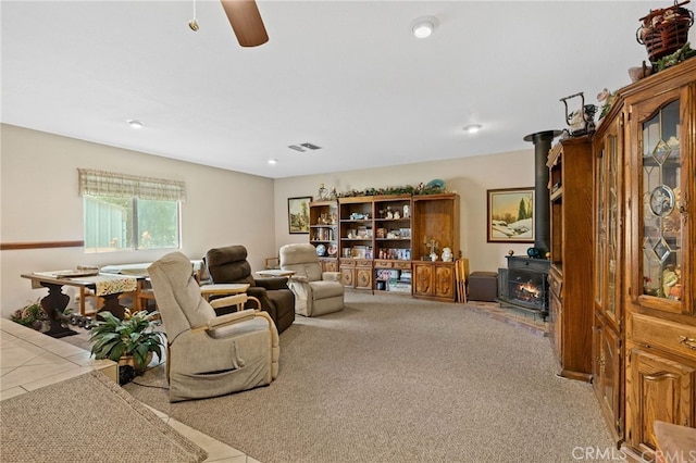 carpeted living room with tile patterned floors, visible vents, a ceiling fan, and a wood stove