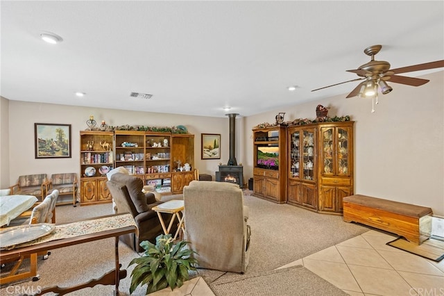 living room featuring visible vents, a wood stove, light tile patterned flooring, ceiling fan, and light colored carpet