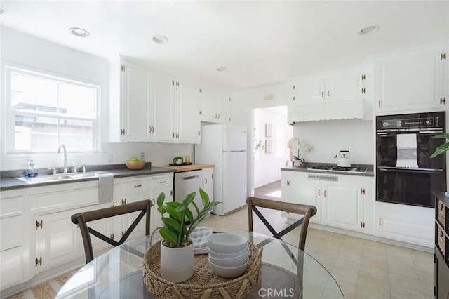 kitchen featuring dobule oven black, freestanding refrigerator, white cabinetry, a sink, and gas cooktop