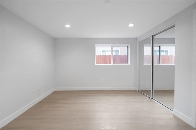 unfurnished bedroom with recessed lighting, a closet, light wood-type flooring, and baseboards