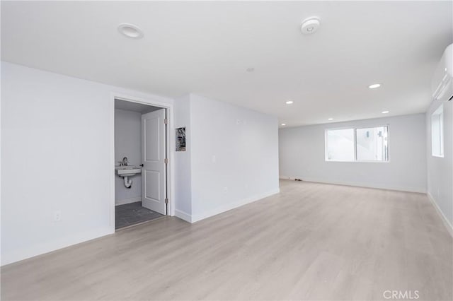 unfurnished room with recessed lighting, a sink, light wood-style flooring, and baseboards