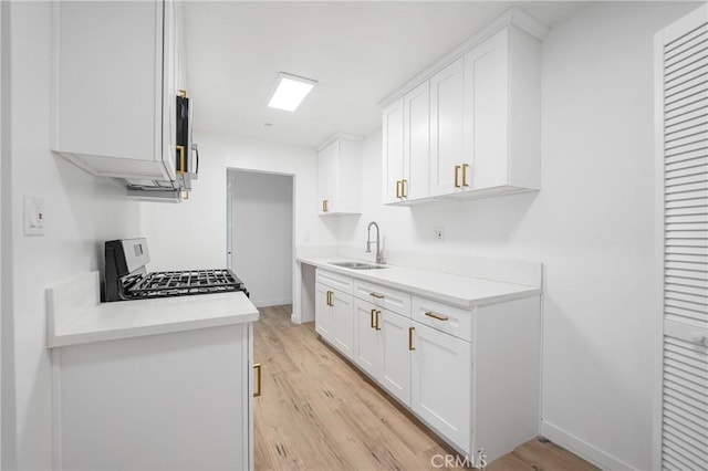 kitchen featuring gas range, light wood-style flooring, light countertops, and a sink