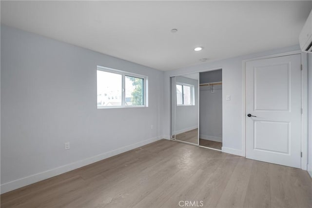 unfurnished bedroom featuring light wood finished floors, baseboards, a wall mounted air conditioner, a closet, and recessed lighting