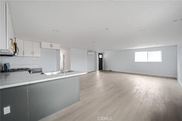 kitchen with a peninsula, white cabinets, light wood-type flooring, range, and stainless steel microwave