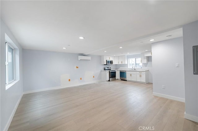 unfurnished living room with light wood-style flooring, recessed lighting, a sink, baseboards, and a wall mounted air conditioner