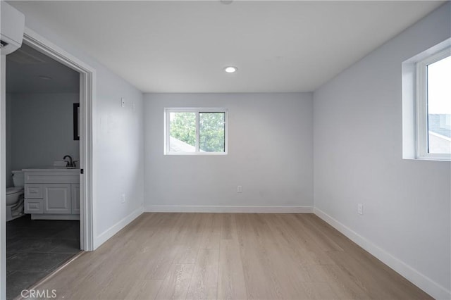 unfurnished room featuring a sink, baseboards, wood finished floors, and a wall mounted air conditioner